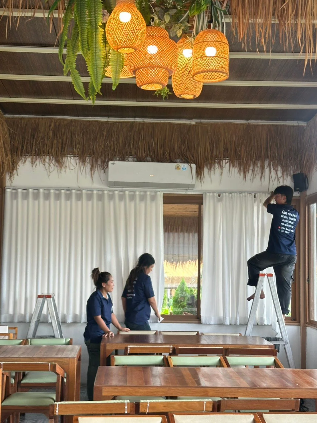 ทีมช่างติดตั้งม่านขาวในร้านอาหารหลังคาจาก ตกแต่งด้วยโคมไม้ไผ่