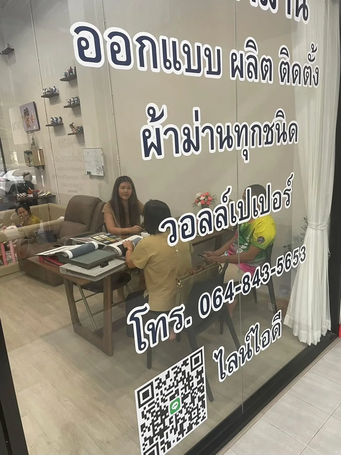 พนักงานร้านนิชา ผ้าม่าน กำลังเปิดเล่มตัวอย่างผ้าให้ลูกค้าดูที่โต๊ะในร้าน