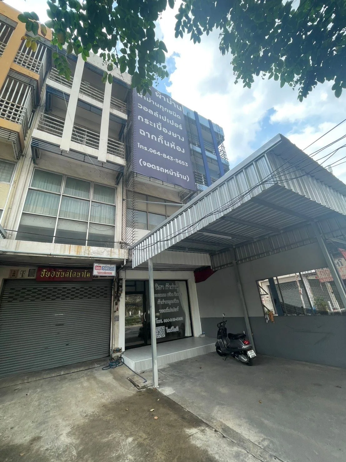 ตัวอาคารร้านนิชา ผ้าม่าน ป้ายร้านระบุบริการและวงเล็บว่าจอดรถหน้าร้าน มีหลังคาเหล็กคลุมที่จอดรถ